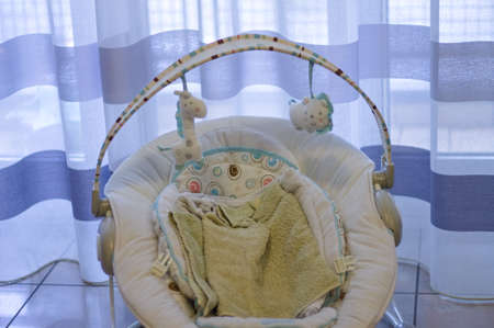 A baby bouncer with toys and towels on the ground in front of a striped curtain in the living room (Marche, Italy, Europe)の写真素材