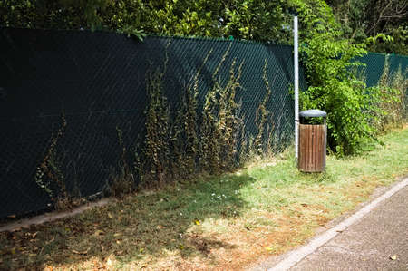 A wooden and metal garbage can on the edge of a pedestrian walkway in a public park (Marche, Italy, Europe)の写真素材