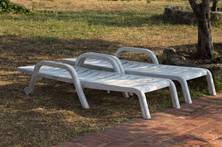 A pair of white plastic sun loungers under the shade of trees in the garden (Umbria, Italy, Europe)