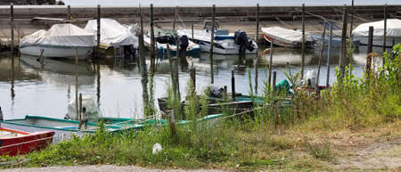 Small motor boats moored on wooden poles of the pier of a small port in Lake Trasimeno (Umbria, Italy, Europe)の写真素材