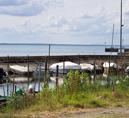 Small motor boats moored on wooden poles of the pier of a small port in Lake Trasimeno (Umbria, Italy, Europe)の写真素材
