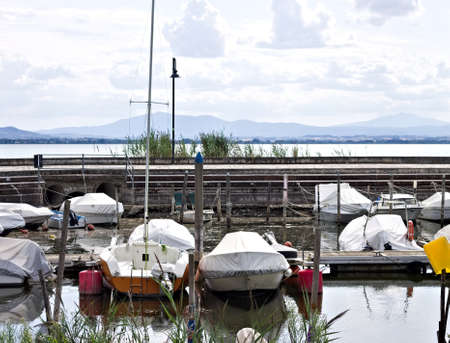 Small motor boats moored on wooden poles of the pier of a small port in Lake Trasimeno (Umbria, Italy, Europe)の写真素材