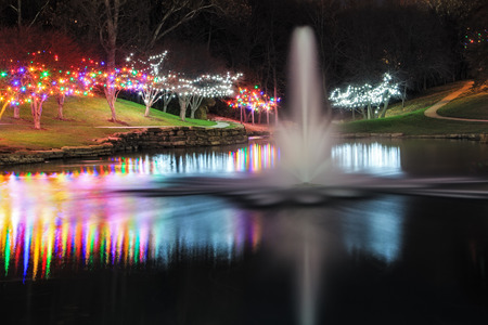 View of a pond with a fountain surrounded by trees with Christmas lightsの写真素材