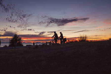 Silhouette of a man and a woman on a bicycle at sunset.の写真素材