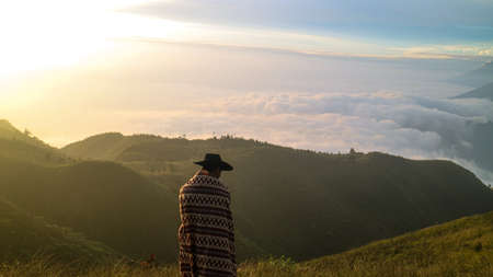 A young man stands with a Beautiful view from the top of Mount Prau, Indonesiaの写真素材