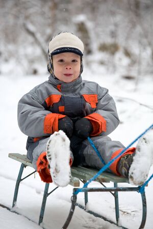 The boy in the winter suit sitting on a old sledge