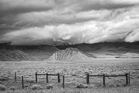 Black and white photo of a fence in the mountains under a cloudy sky in Wyoming.の写真素材