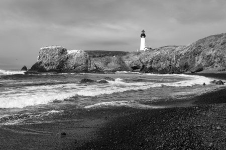 Black and white image of the Yaquina Head central Oregon Pacific coast lighthouse on a black sand beach.の写真素材