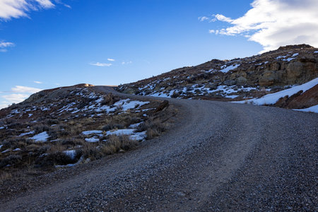 Winding road in the mountains with snow on the ground and blue skyの写真素材