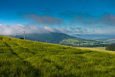Summer field under cloudy sky in mountains during morningの写真素材