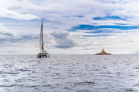 Catamaran yacht sailing in Adriatic with watchtower in backgroundの写真素材