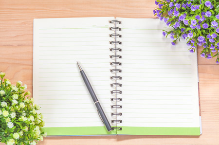 Spiral notebook with pen and flowers on wood backgroundの写真素材