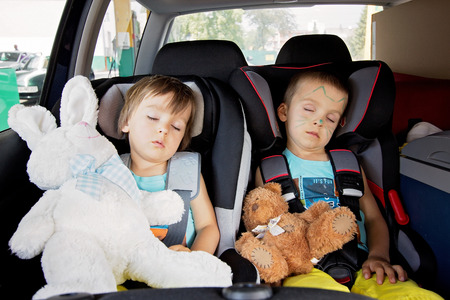 Two boys in car seats, travelling, sleeping in the car with teddy bearsの写真素材