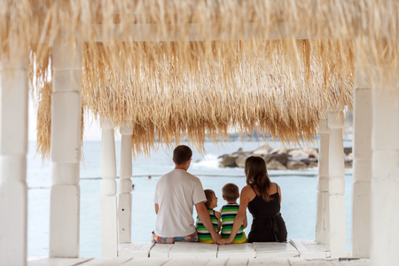 Back view of a happy family, sitting on the beach, watching the sea togetherの写真素材