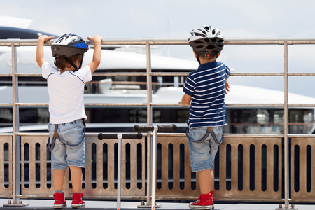 Two cute boys with scooters, looking at big boat on the port in Monacoの写真素材