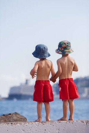 Two boys, contemplating a big ship in the sea, standing on a wallの写真素材