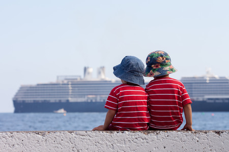 Two boys, contemplating a big ship in the sea, sitting on a wallの写真素材