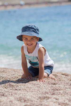 Cute boy, playing with pebbles on the beach in the morningの写真素材