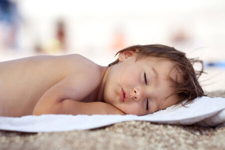 Adorable baby boy, sleeping on the beach, exhausted after fun day at the beachの写真素材