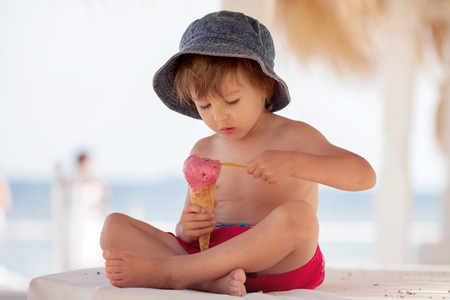 Cute shirtless boy, eating red ice cream on the beachの写真素材