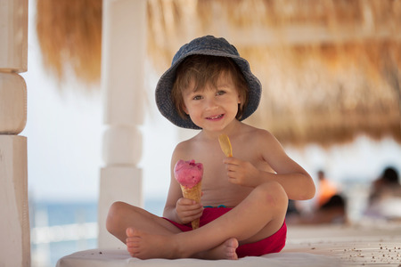 Cute shirtless boy, eating red ice cream on the beachの写真素材