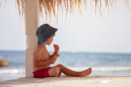 Cute shirtless boy, eating red ice cream on the beachの写真素材