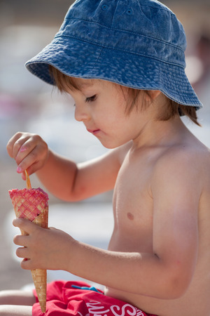 Cute shirtless boy, eating red ice cream on the beachの写真素材