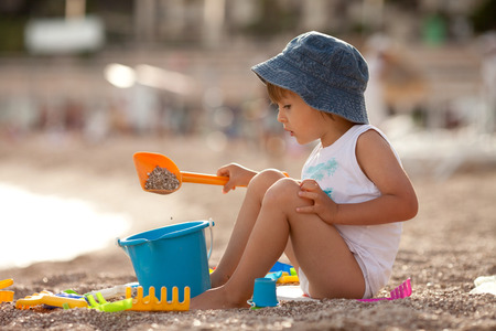 Adorable happy boy, playing with toys on the beach, sunset timeの写真素材