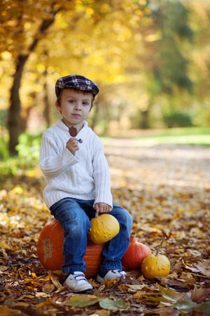 Boy in a park, sitting on a pumpkin, eating chocolate lollypopの写真素材