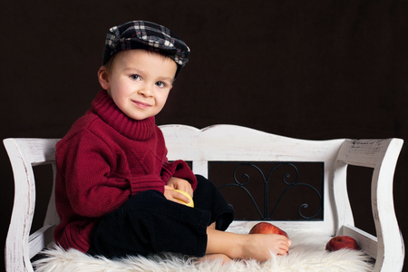 Boy, sitting on a bench, holding apple, indoor shotの写真素材