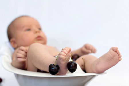 Baby boy in a bowl with cherries の写真素材