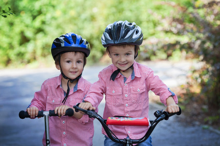 Portrait of two boys in the park, riding bike and scooter, smiling at the cameraの写真素材
