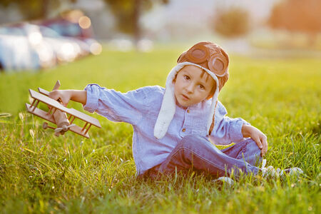 Cute boy, playing with airplane on sunset in the park, smiling