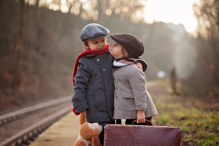 Two boys on a railway station, waiting for the train with suitcase and teddy bearの写真素材