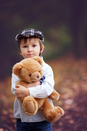 Little boy with suitcase and teddy bear in park, having funの写真素材