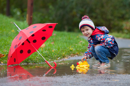 Cute boy with hat, playing with rubber ducks in the park in a puddleの写真素材