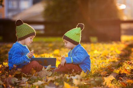 Two boys, reading a book on a lawn in the afternoon, eating snacks, autumn sunset timeの写真素材