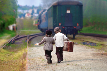 Two boys, dressed in vintage clothing and hat, with suitcase, on a railway stationの写真素材