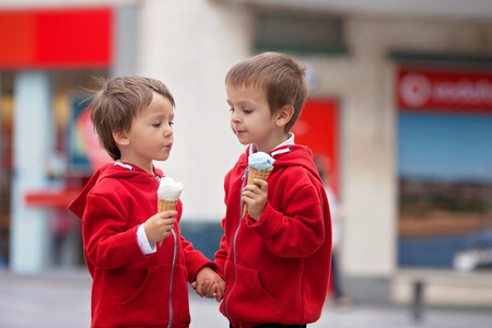 Two cute boys, eating ice cream on the street, tasting each others ice creamの写真素材