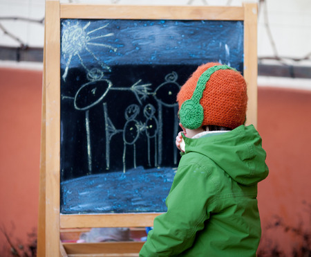 Adorable little boy, drawing summer picture with chalk on a board on a winter dayの写真素材