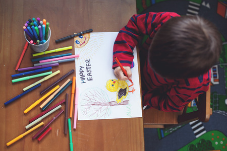 Adorable little boy, drawing picture for easter at home, having fun, smiling at camera, shot from aboveの写真素材