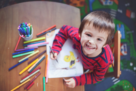 Adorable little boy, drawing picture for easter at home, having fun, smiling at camera, shot from aboveの写真素材