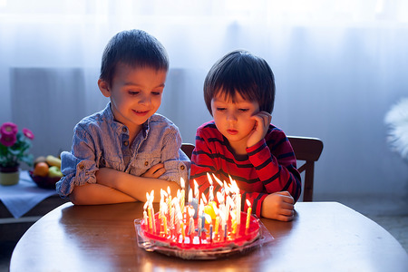 Adorable cute boys, blowing candles on a birthday cake at homeの写真素材