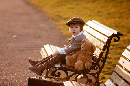 Adorable little boy with his teddy bear friend in the park on sunset, nice back lightの写真素材