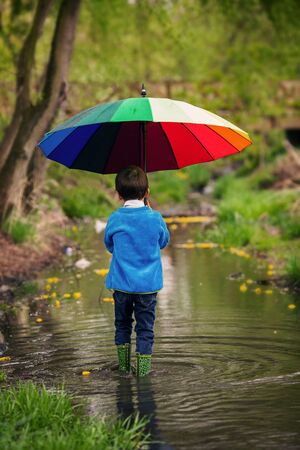 Cute little boy, walking in a pond on a rainy day, playing and jumping, smiling, springtimeの写真素材