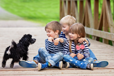 Three beautiful adorable kids, siblings, playing with cute little dog in the park, springtimeの写真素材