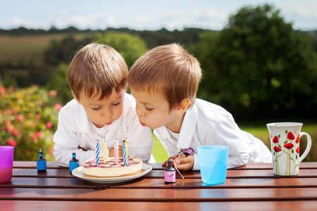 Adorable boys, blowing candles on a birthday cake in the garden, outdoorの写真素材