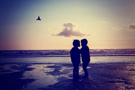 Silhouette of two kids, kissing on the beach, seagull frying over themの写真素材