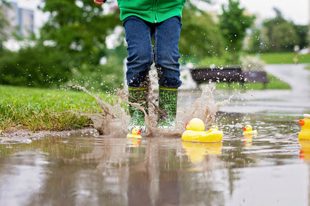 Little boy, jumping and playing in muddy puddles in the park, rubber ducks in the puddleの写真素材
