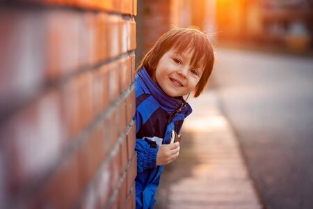 Adorable little boy, next to brick wall, eating chocolate bar on sunset, springtimeの写真素材